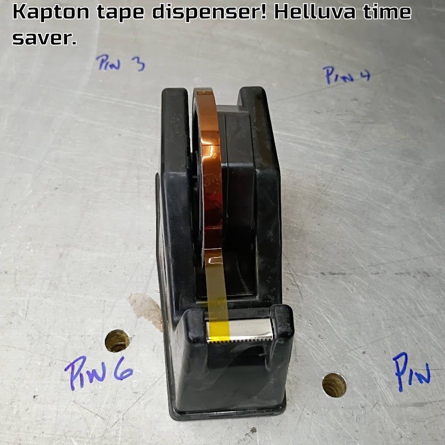 Black Kapton tape dispenser with amber tape on a gray workbench.