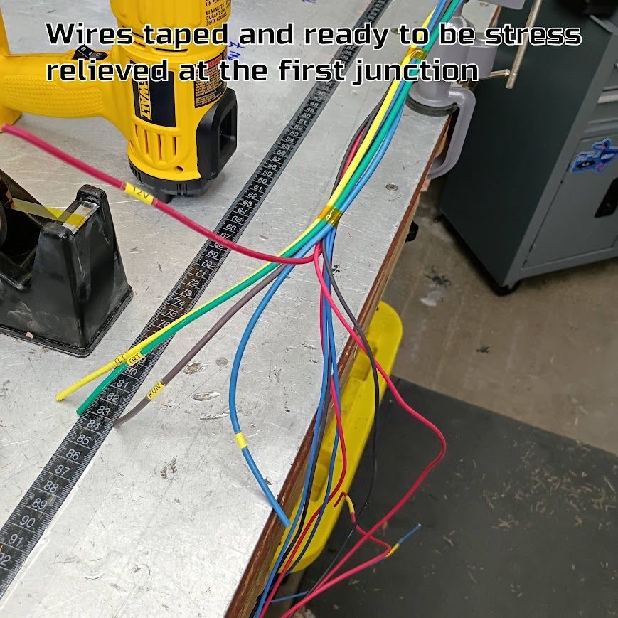 Color-coded wires taped and routed over a workbench near a yellow drill, ready for stress relief.