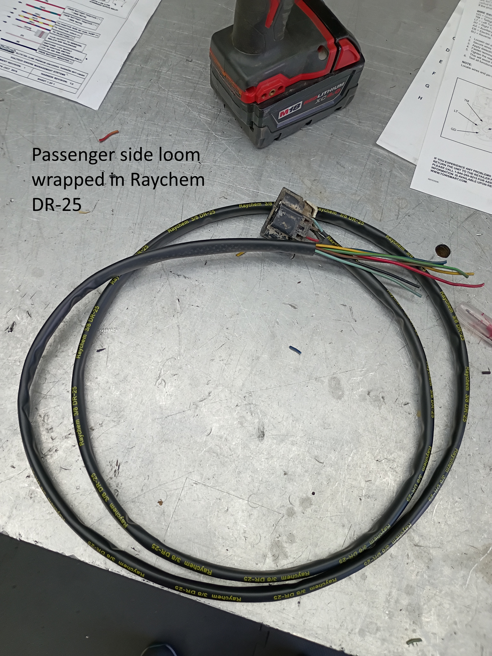Coiled black cable on concrete floor beside red battery pack and note labeled “Passenger side MBR wrapped in Raychem DH-25”