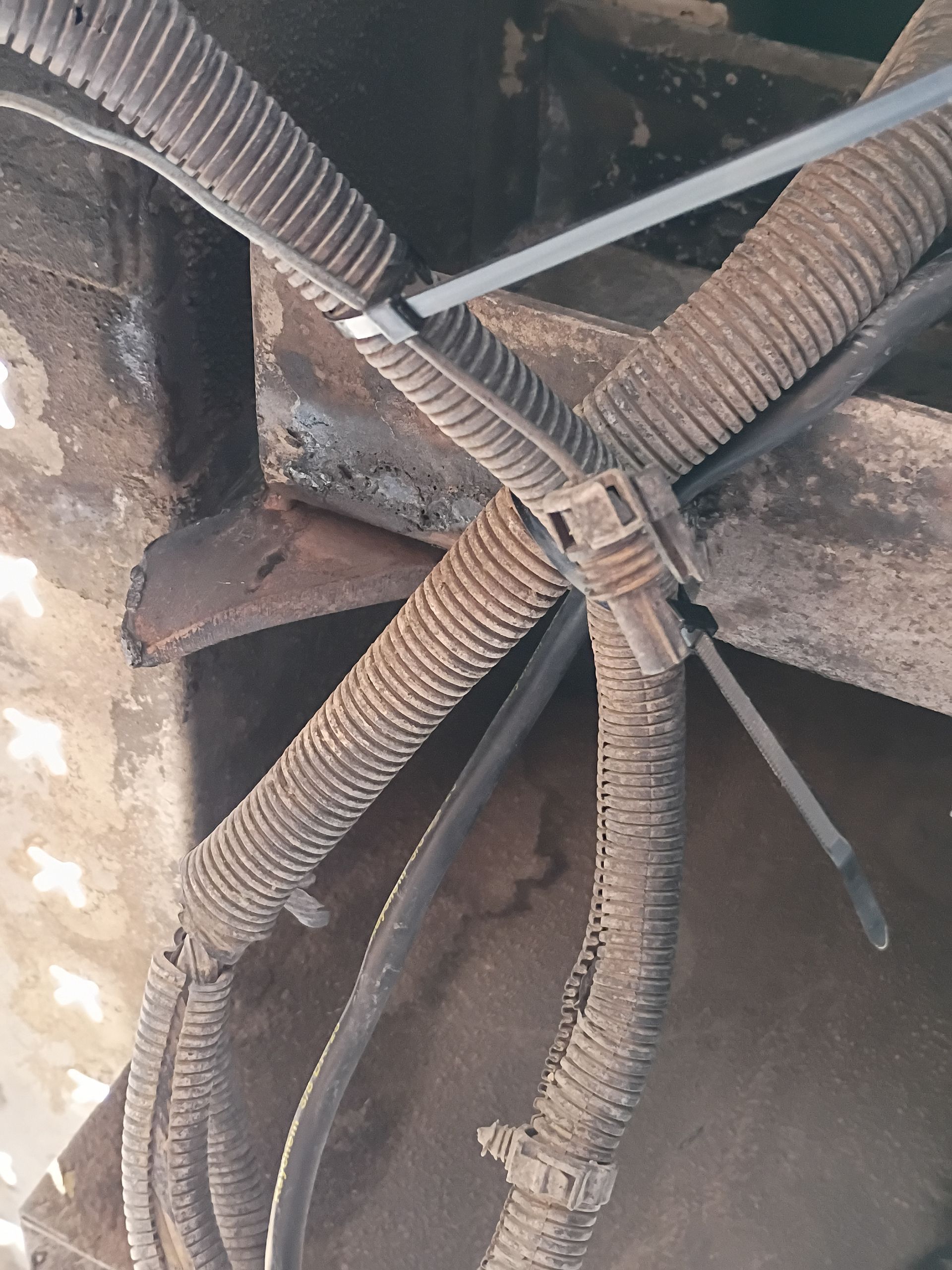 Frayed electrical wires bundled with zip ties inside a dusty metal compartment