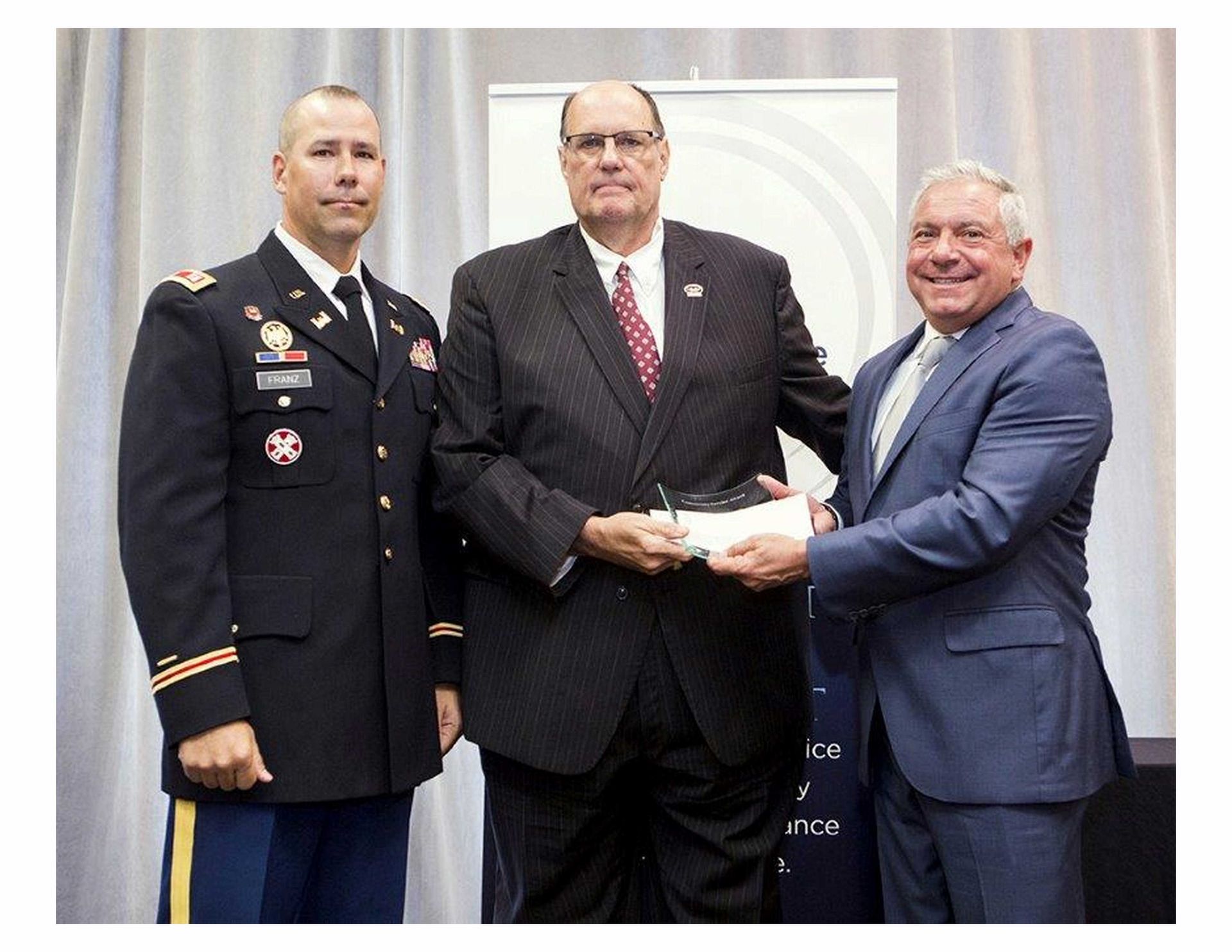 A man in a military uniform stands between two men in suits