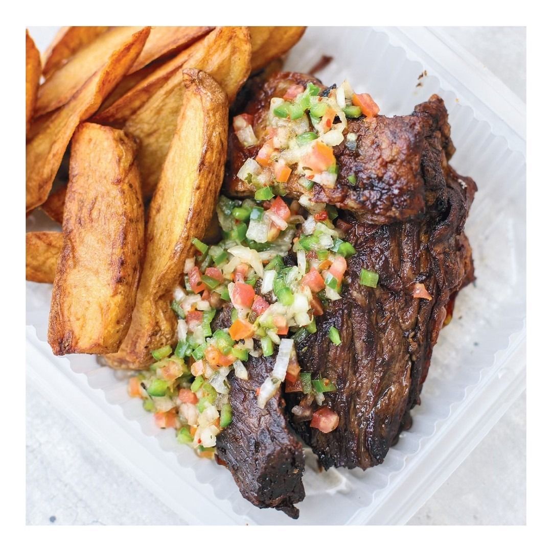 Carne a la parrilla con pico de gallo y papas fritas gruesas en un envase para llevar.