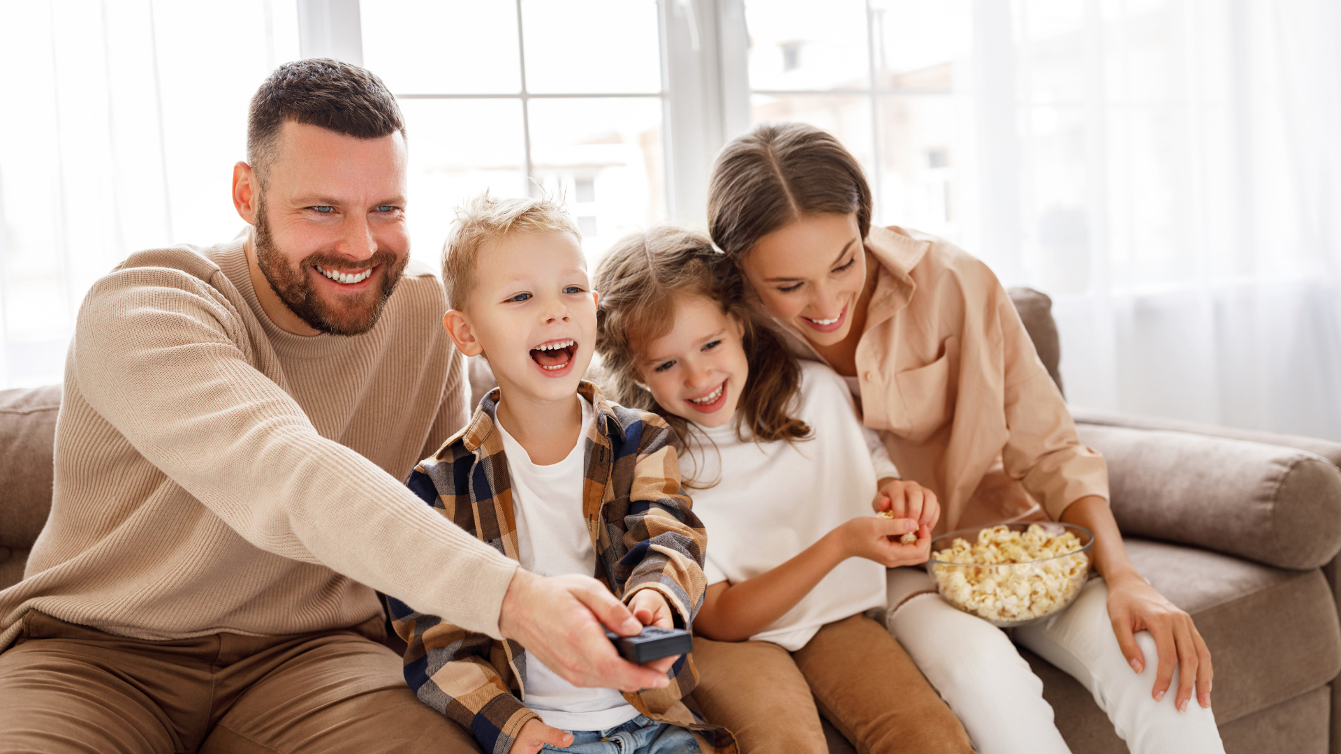 Family sitting on a couch, smiling and eating popcorn while watching TV