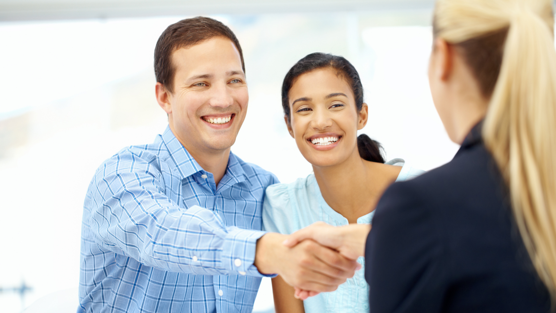Two people smiling and shaking hands with a businesswoman in a bright office setting