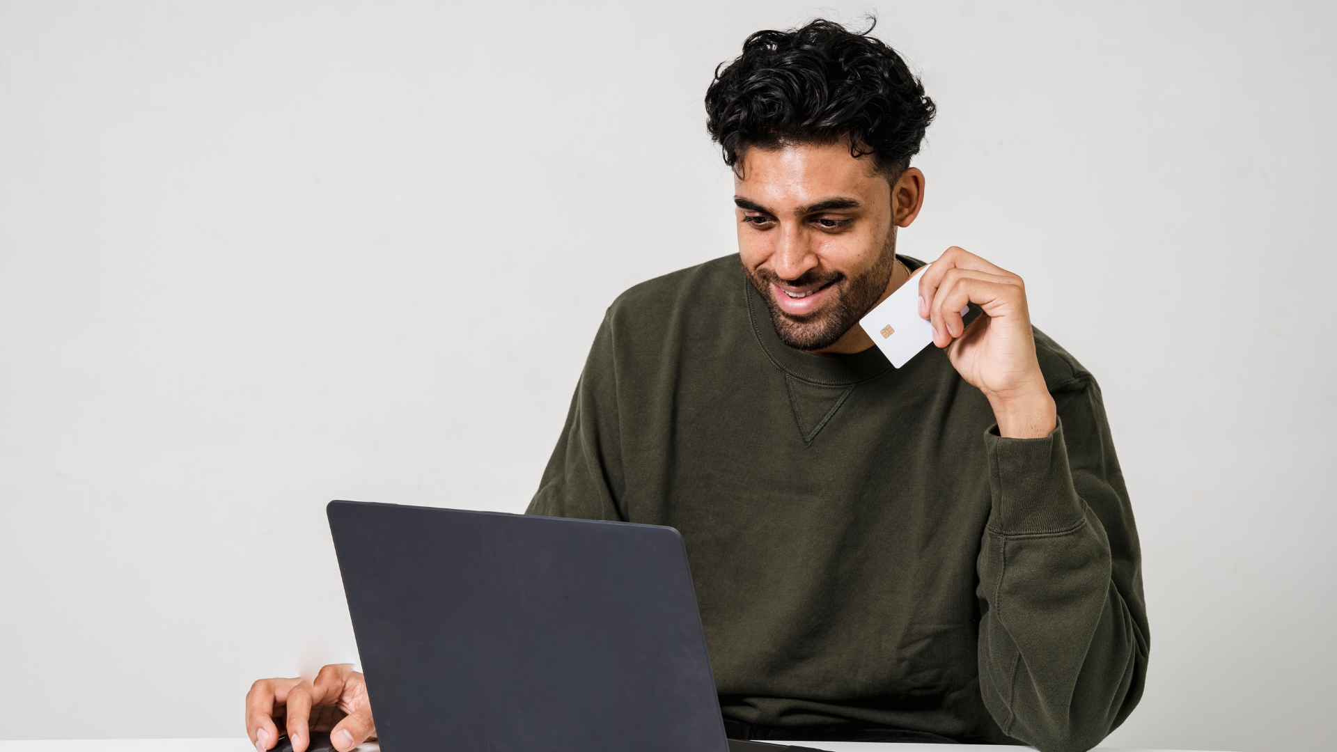 A man is holding a credit card while using a laptop computer.