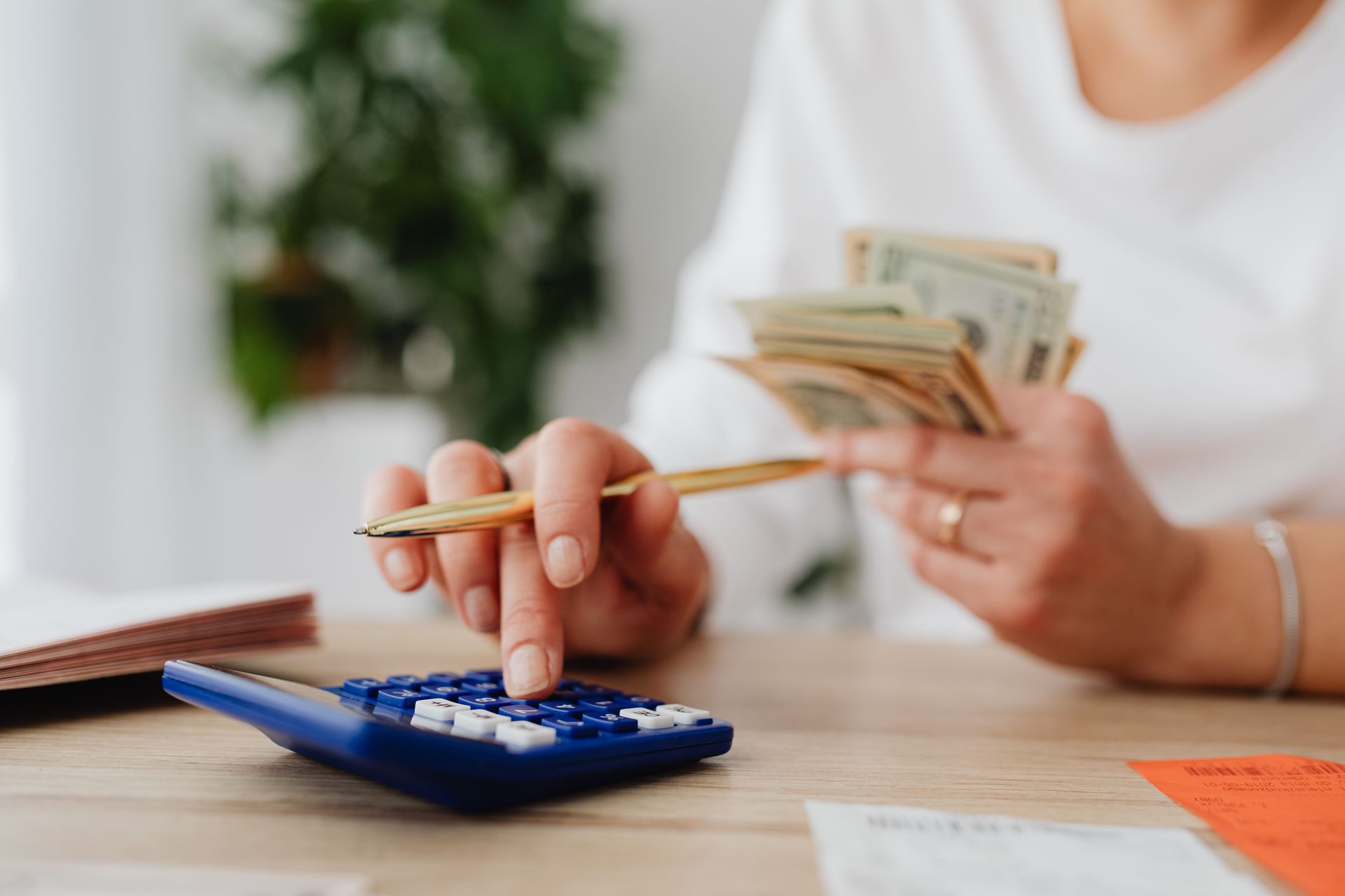Person counting cash beside a blue calculator on a desk, with bills and receipts nearby