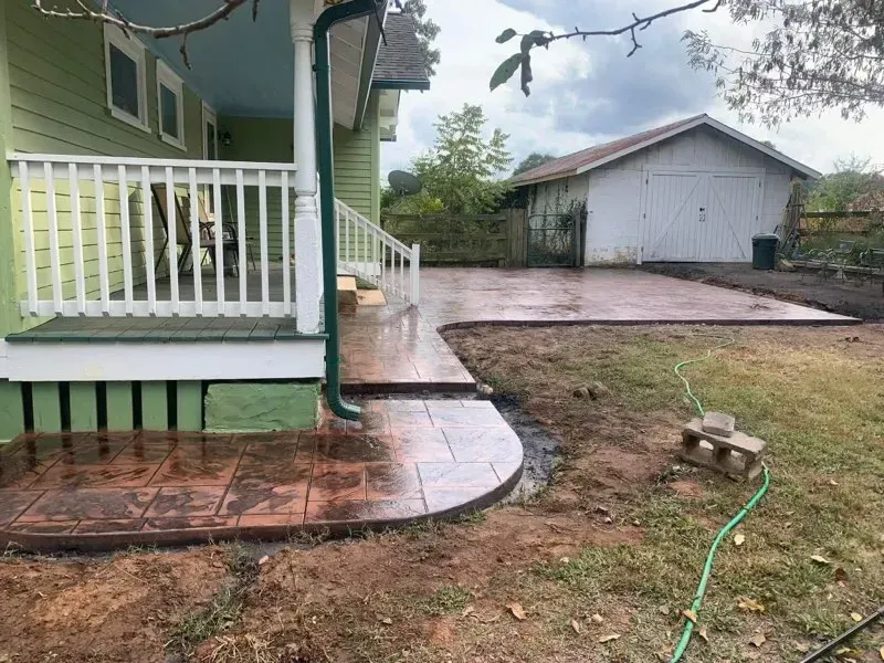 A green house with a white porch and a concrete walkway in front of it.