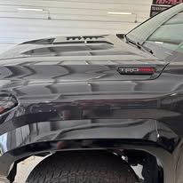 Close-up of a dark gray Toyota truck fender with TRD badge in a garage.