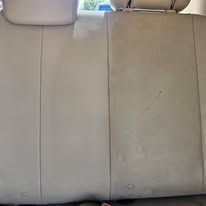Beige leather car back seat with three headrests and visible wear marks
