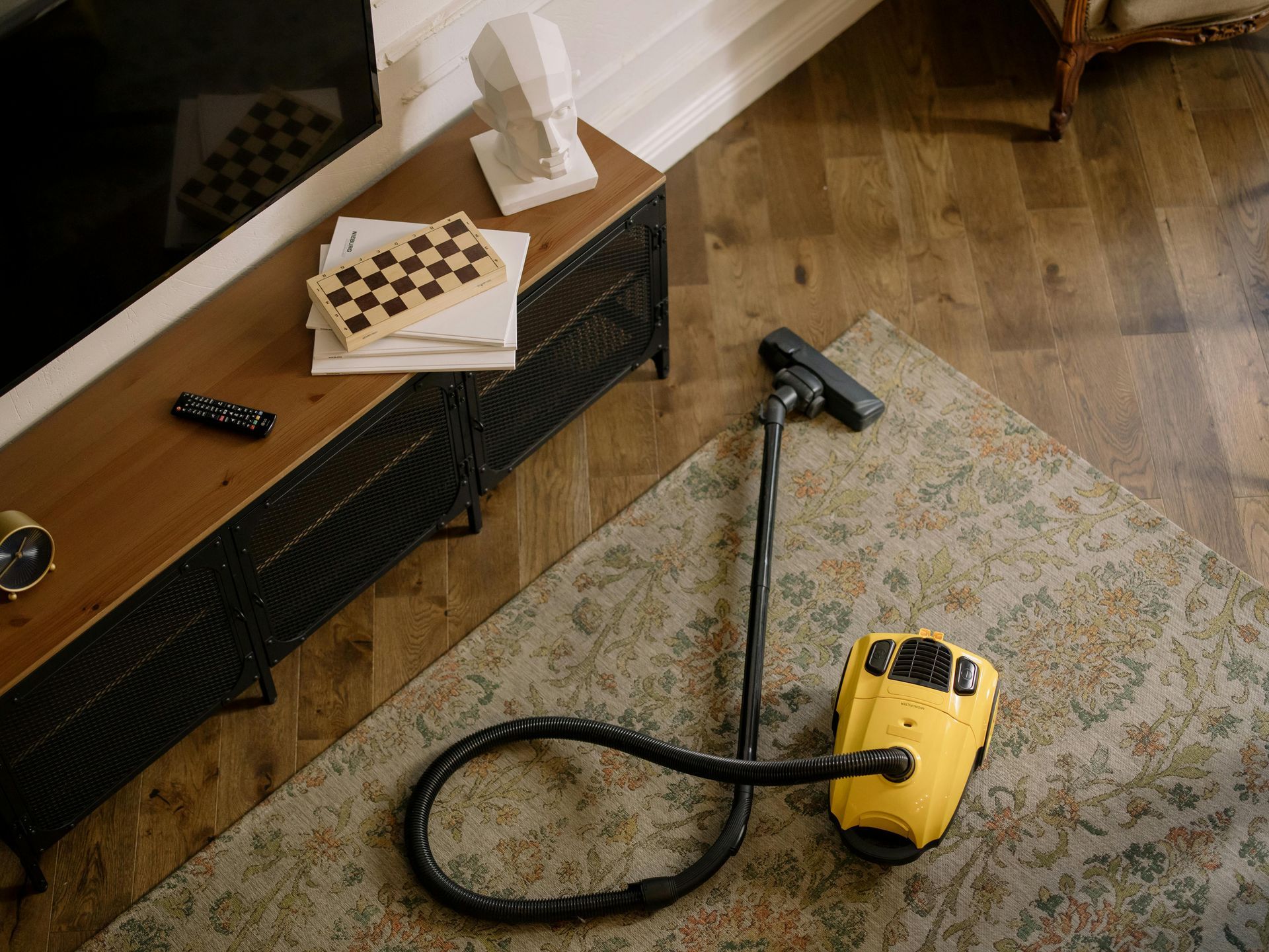 Yellow vacuum lying on a rug next to a black handheld tool and a wooden cabinet