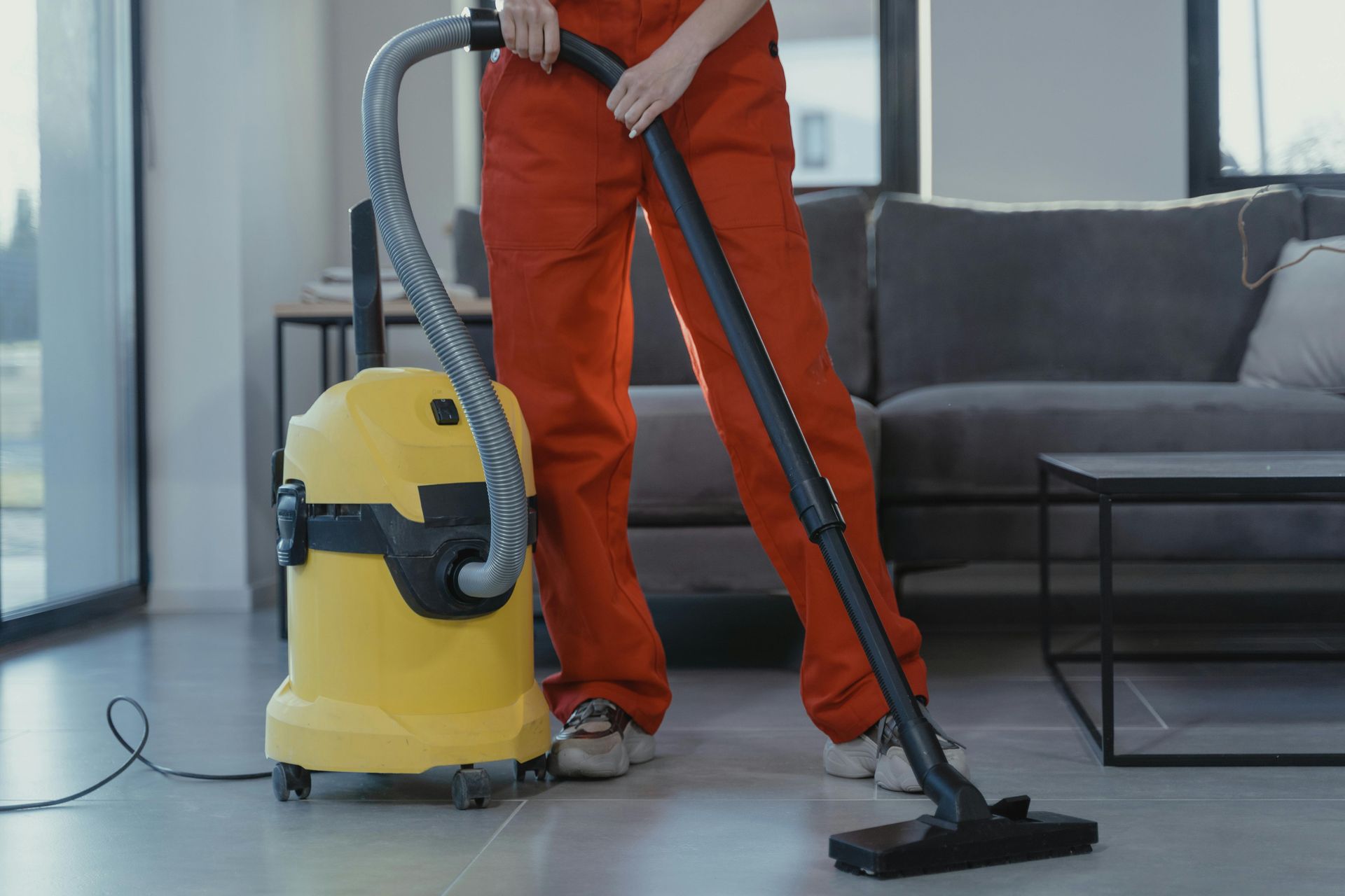 Person vacuuming a living room with a yellow canister vacuum and black floor nozzle