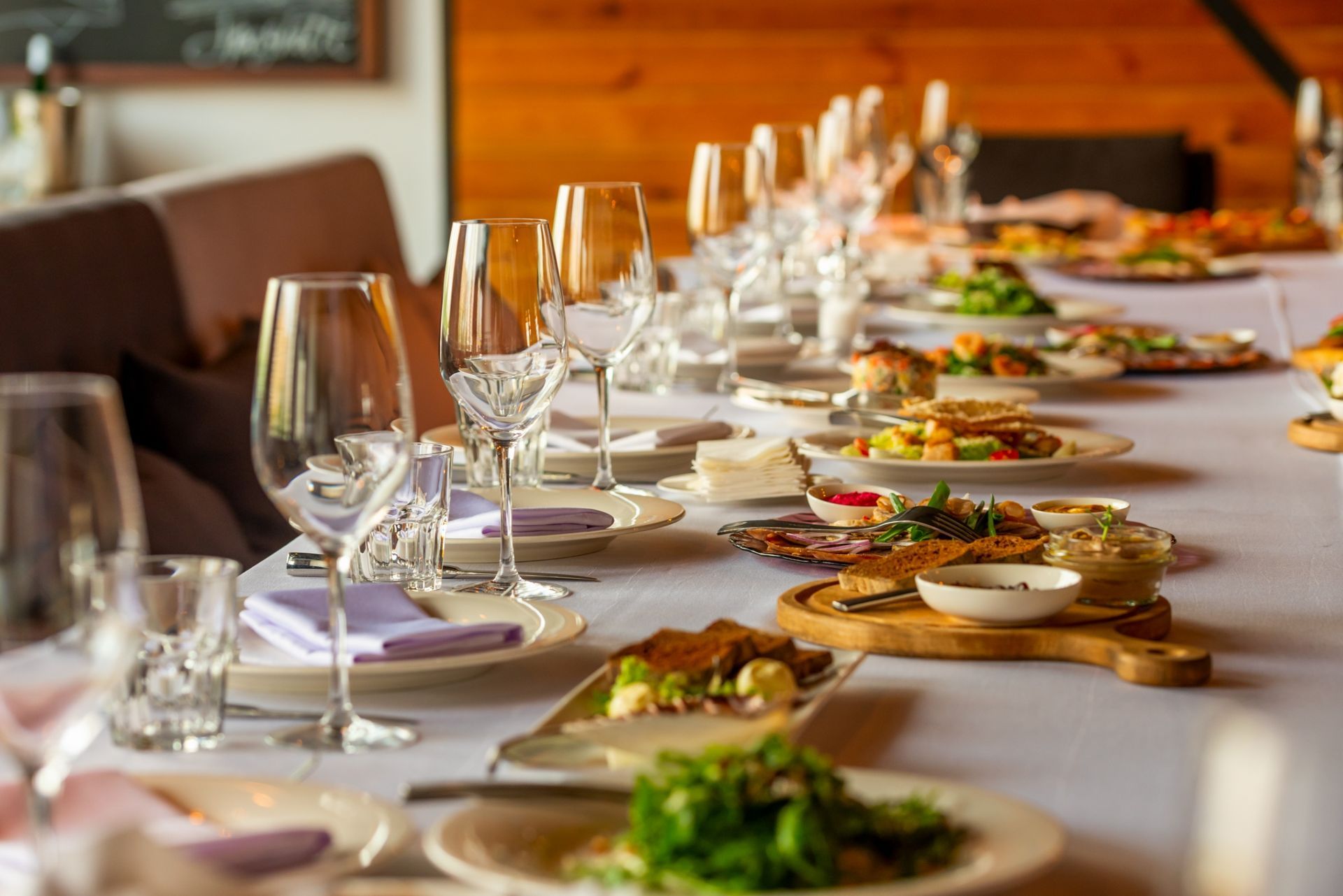 A long dining table set for a formal meal with wine glasses, white napkins, and plates of food on a white tablecloth.