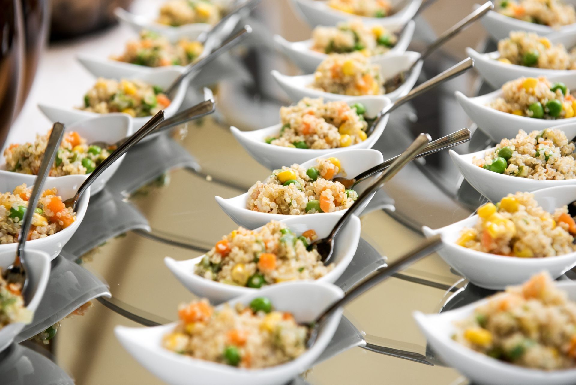 Small white bowls of vegetable fried rice with individual spoons arranged on a reflective serving tray.