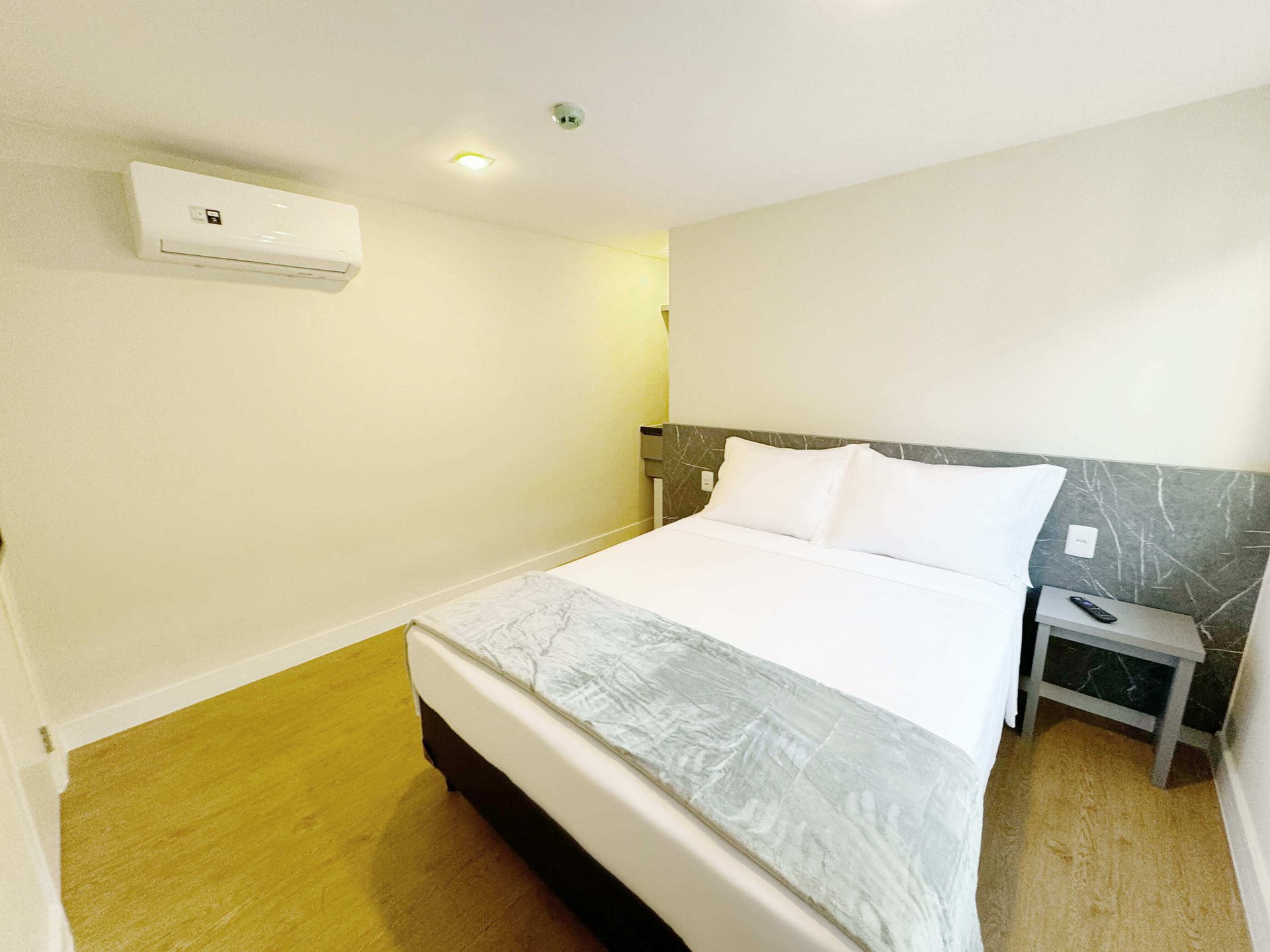 Um quarto de hotel com cama, mesa de cabeceira e ar condicionado.