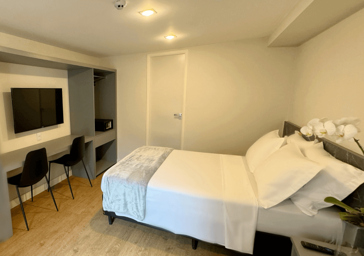 Um quarto com uma cama, escrivaninha, cadeiras e uma TV de tela plana.