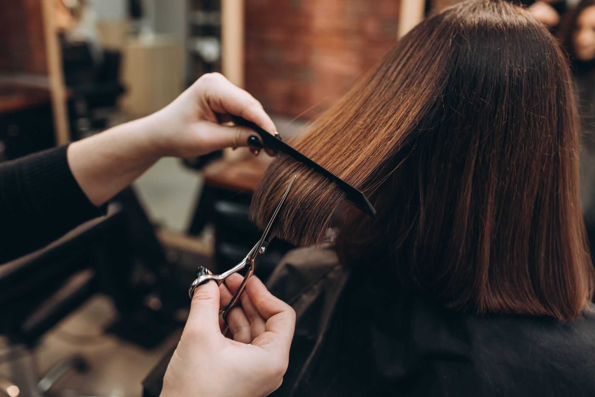 Stylist cutting straight brown hair with scissors in a salon