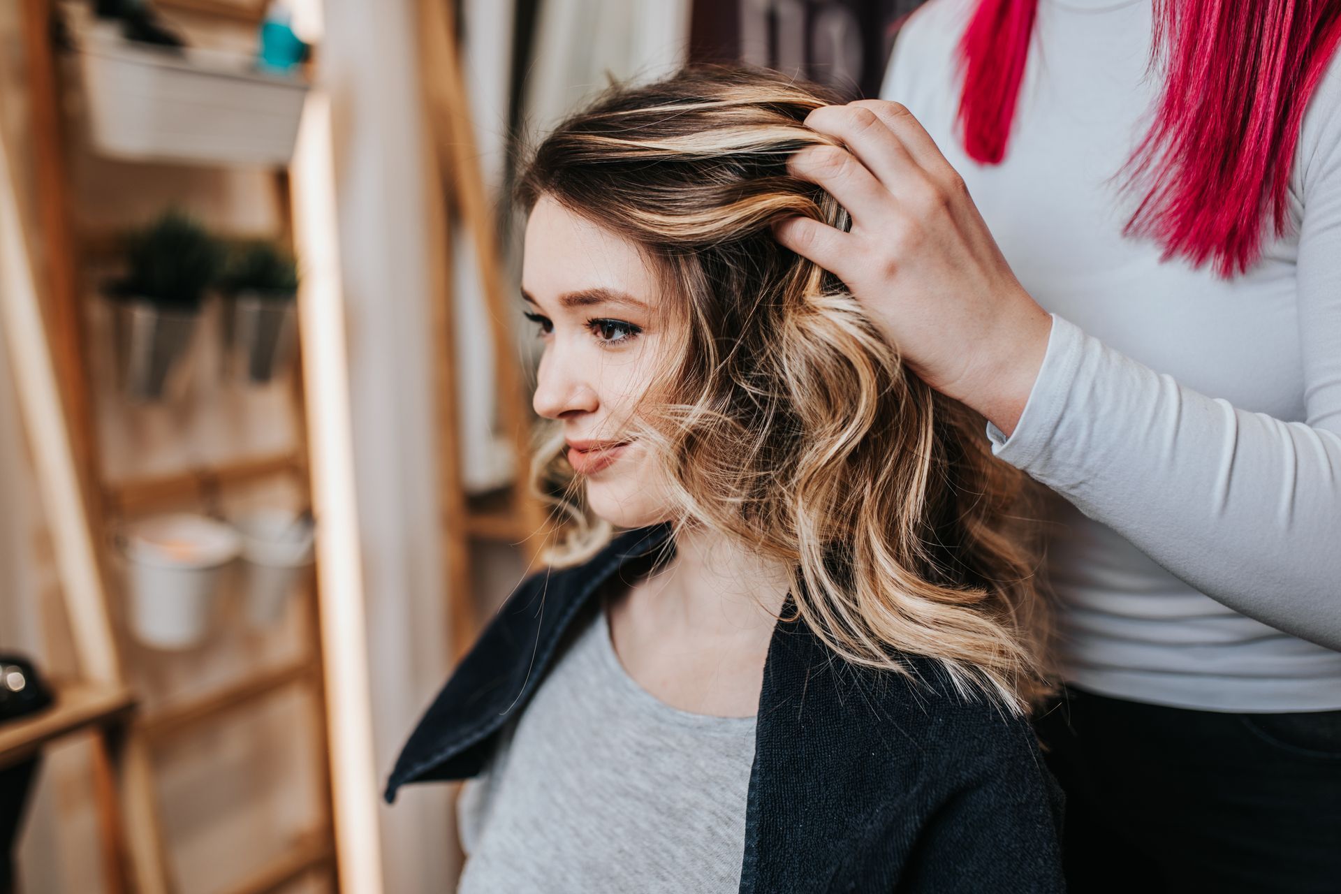 Stylist curling a woman’s hair in a salon chair, with a mirror and red decor in the background