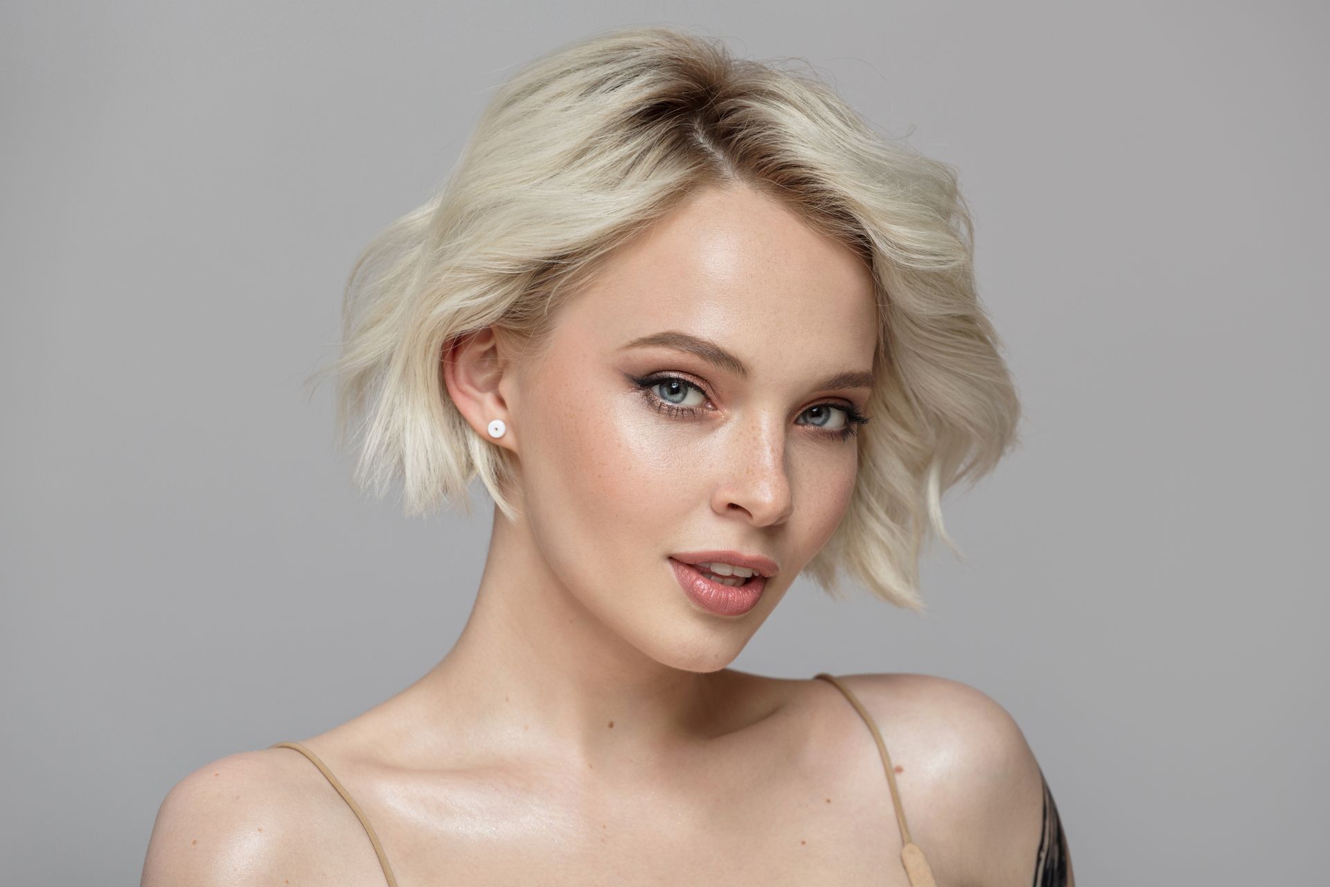 Portrait of a blonde person with short hair against a gray background, wearing a sleeveless top