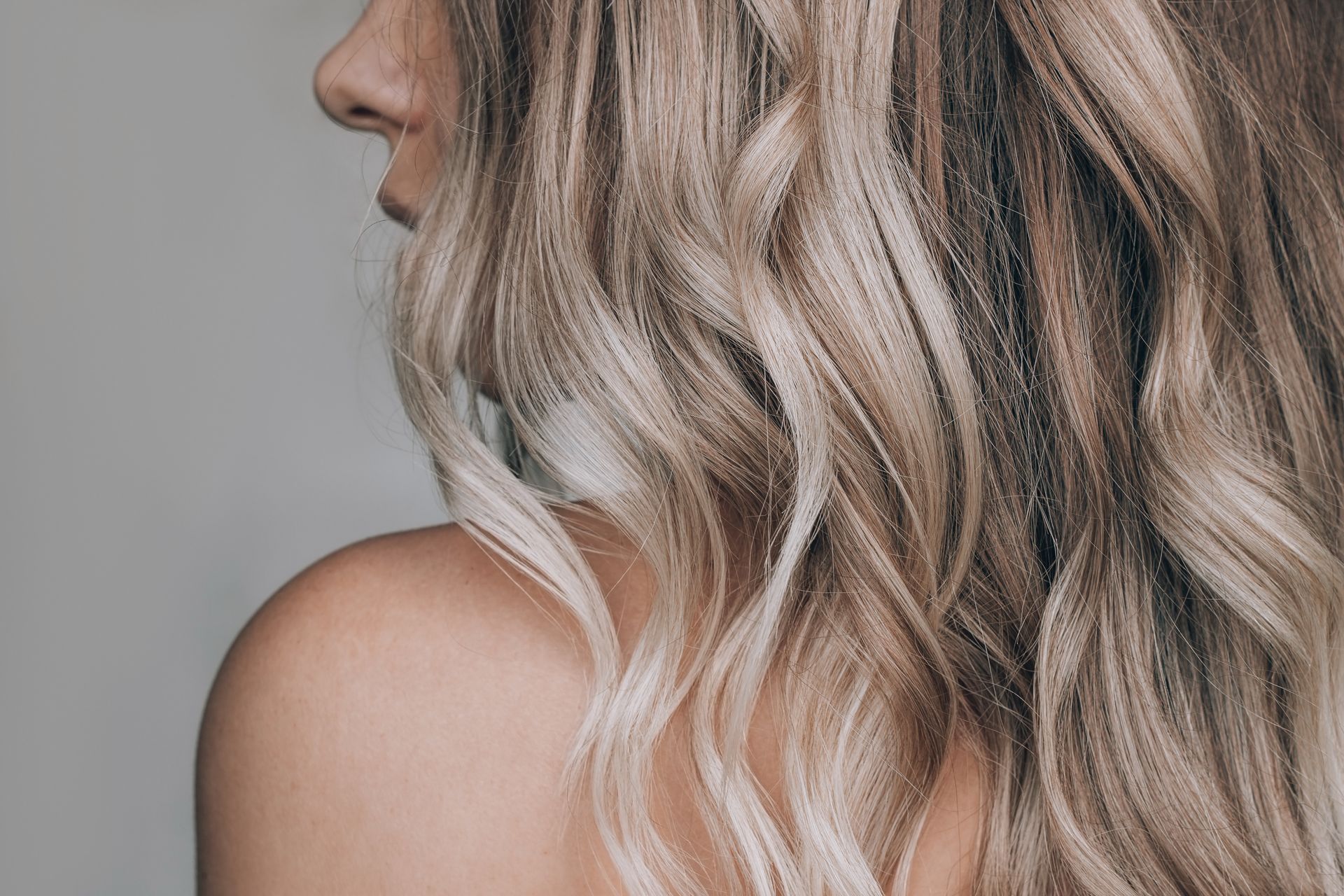 Close-up side view of wavy blonde hair and bare shoulder against a gray background