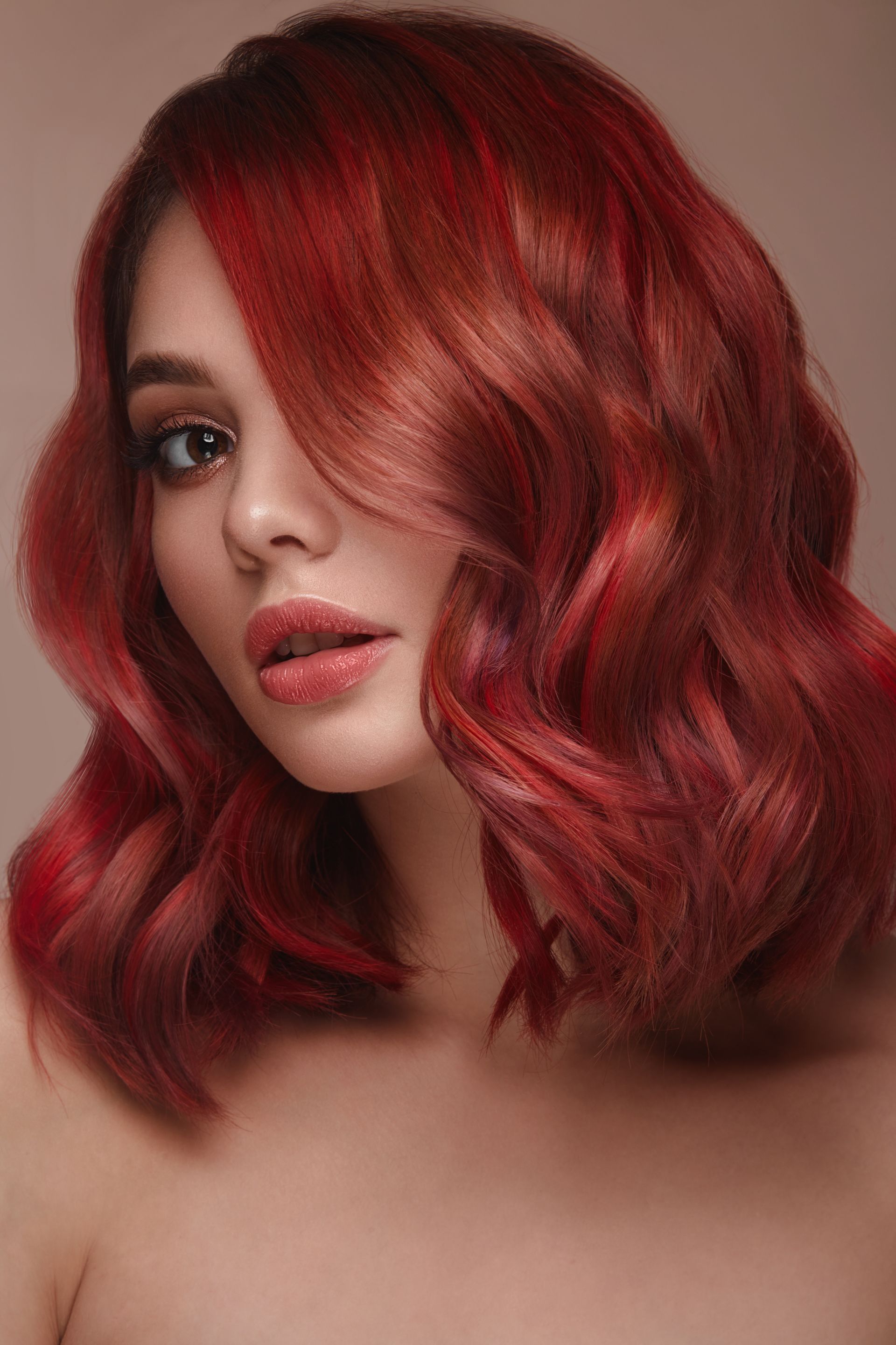 Portrait of a person with wavy red hair and matching makeup against a soft beige background