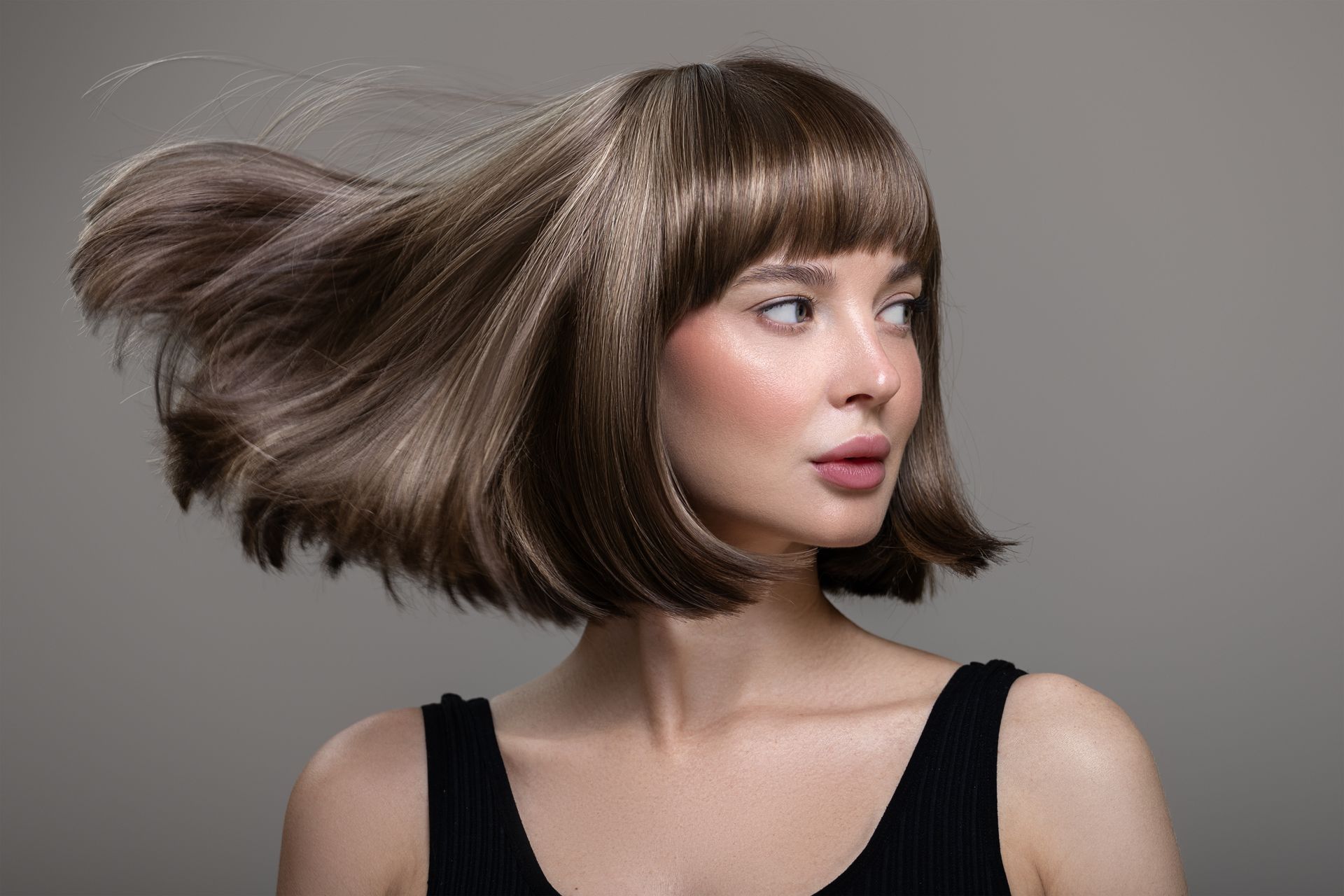 Woman with a short brown bob hairstyle, hair swept dramatically to the left, on a gray background