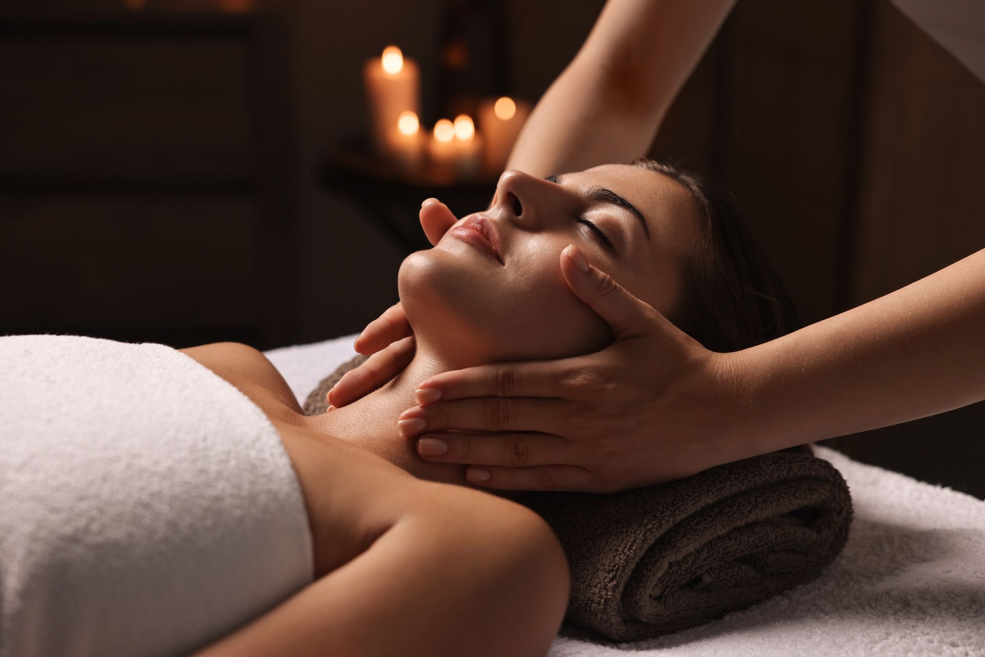 Person receiving a facial massage with hands on face in a spa, candlelight in the background