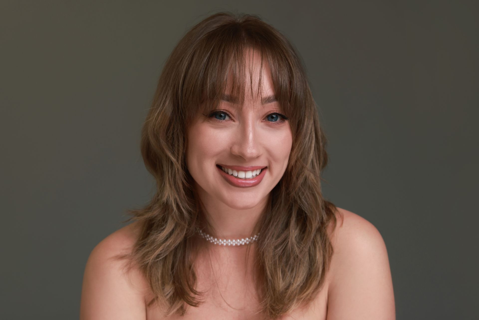 Smiling woman with shoulder-length brown hair against a plain gray background