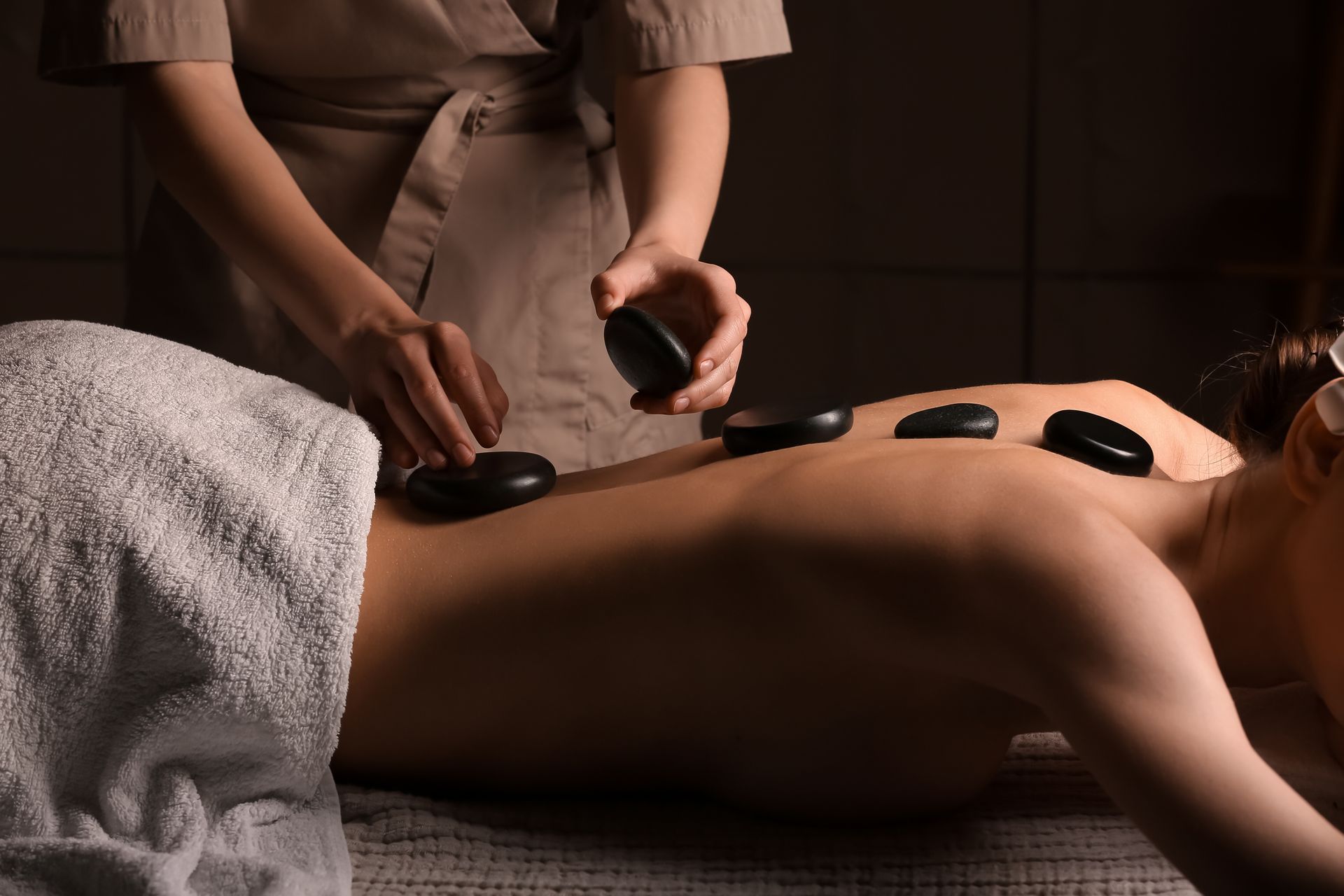 Massage therapist placing hot stones on a client’s back in a spa setting
