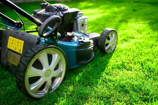 A teal lawn mower sits on a vibrant green lawn on a sunny day. A teal lawn mower sits on a vibrant green lawn on a sunny day.