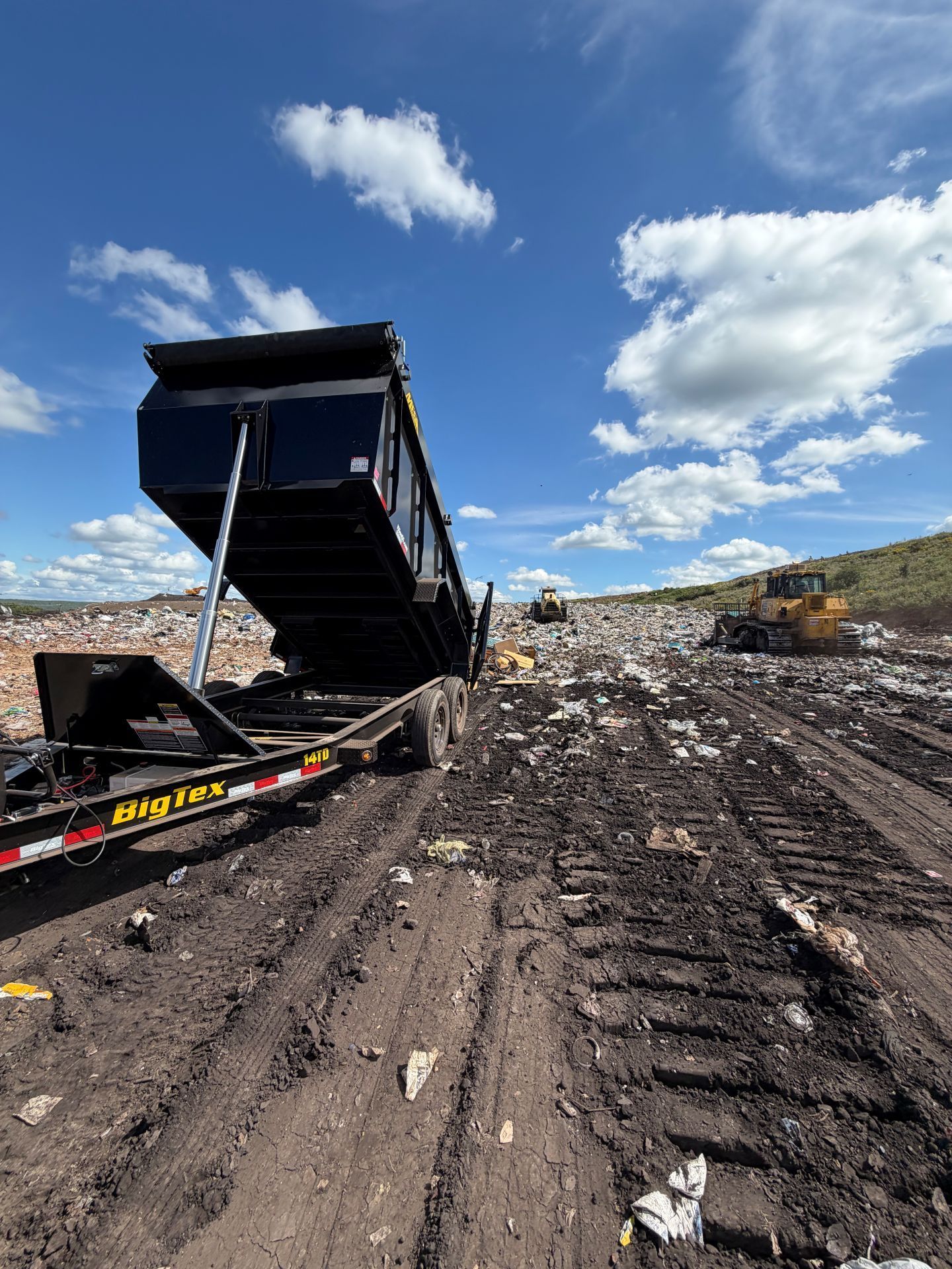 Dump truck tipping debris in a landfill under a blue sky with clouds