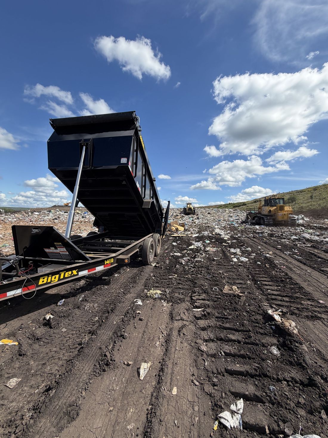 Dump truck unloading debris at a landfill under a blue sky with clouds