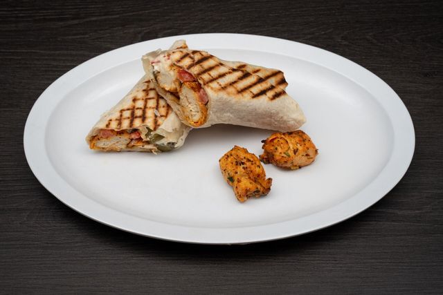 A white plate topped with a grilled wrap and chicken pieces.