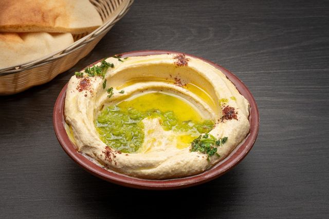 A bowl of hummus is sitting on a table next to a basket of pita bread.