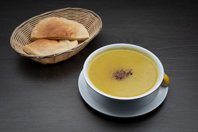 A bowl of soup next to a basket of pita bread