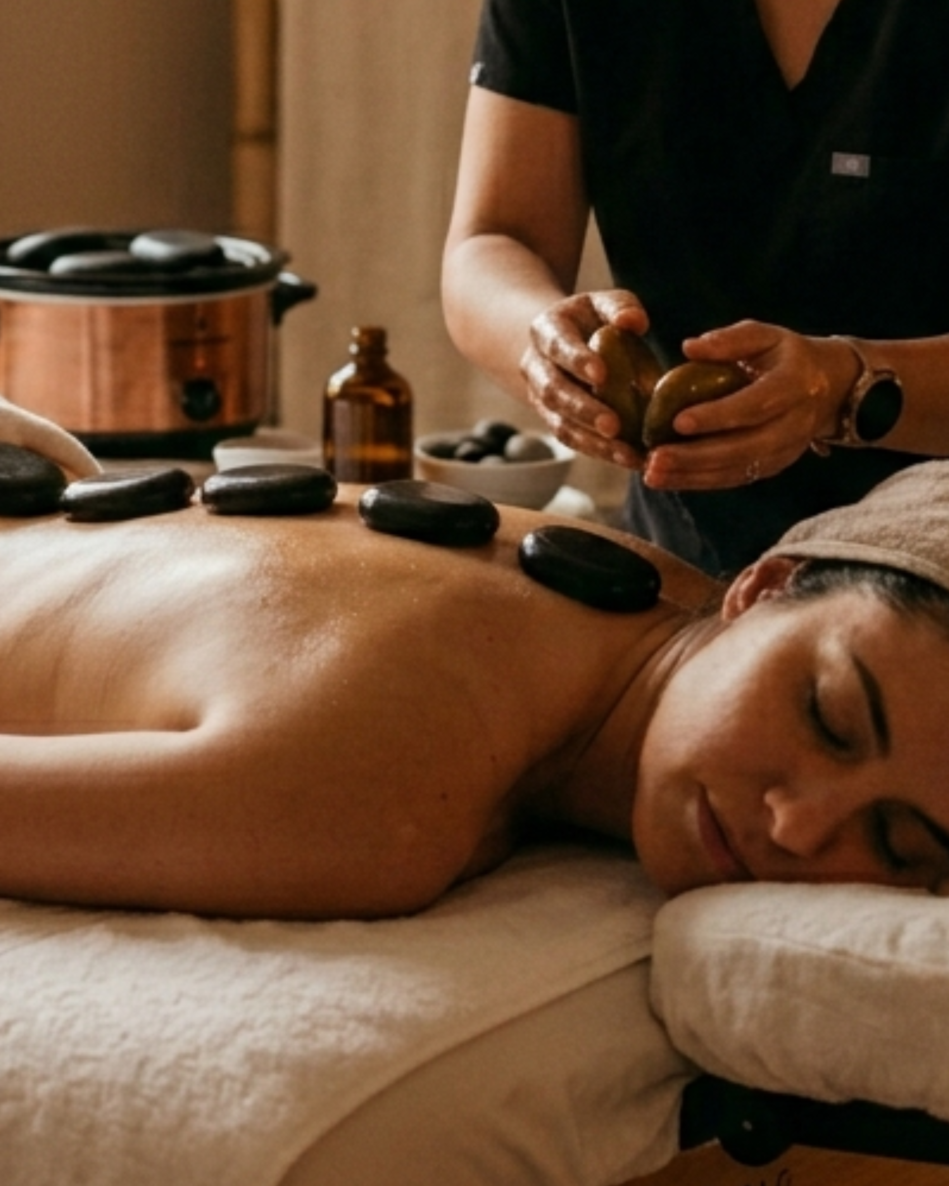 Durante un tratamiento de spa, un masajista coloca piedras lisas, oscuras y calientes sobre la espalda del cliente.