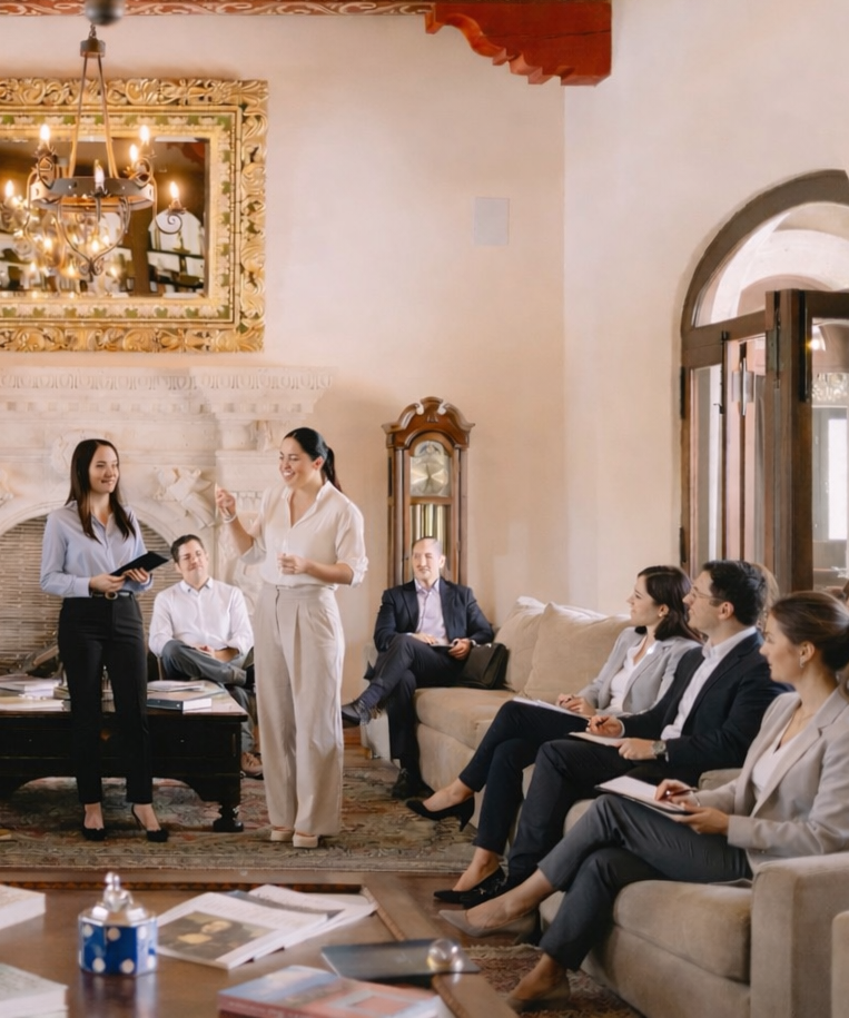 Un orador se dirige a un grupo sentado en un entorno de oficina formal con una decoración elegante y una chimenea.