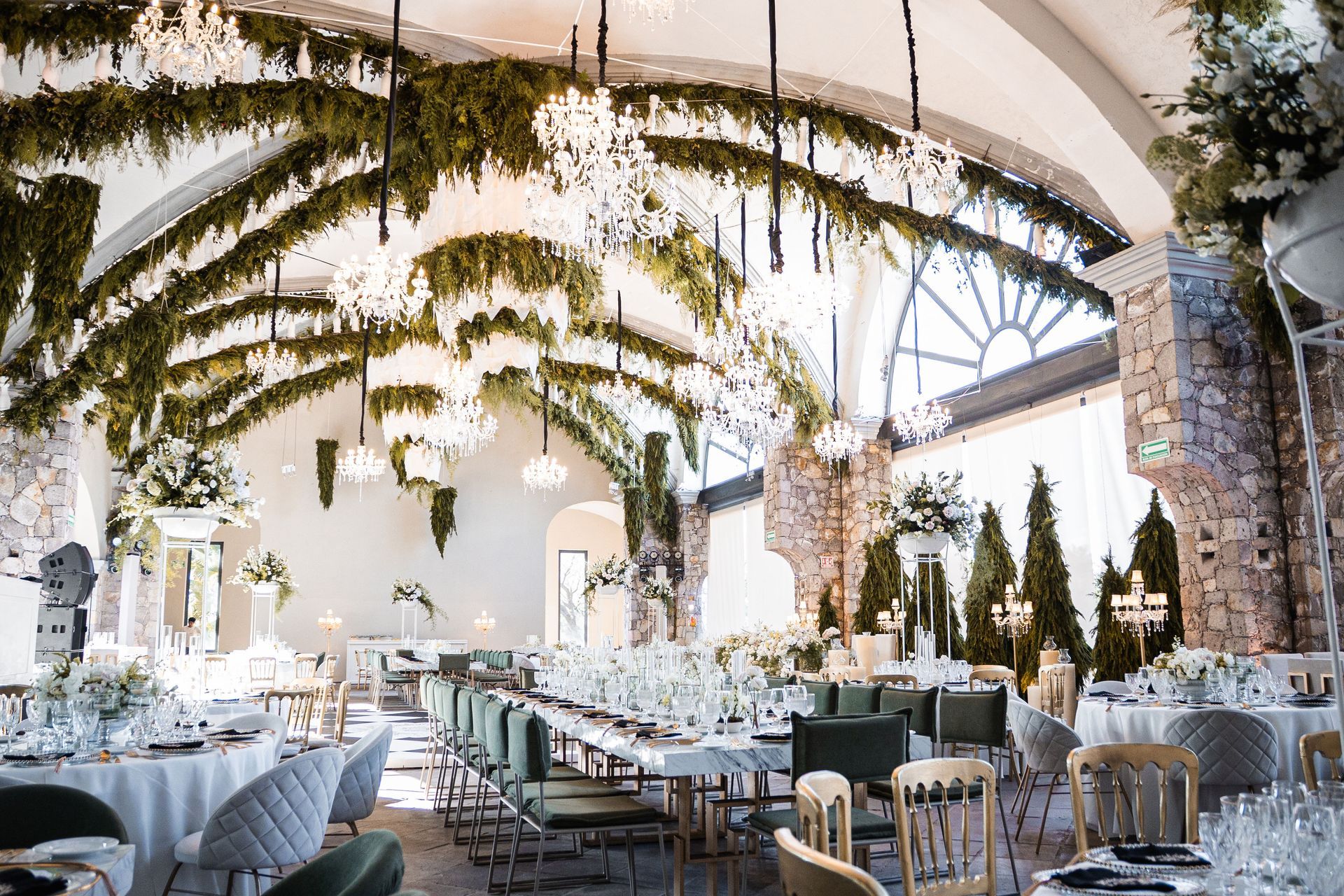 Recepción de boda bajo bóvedas de piedra, con candelabros de cristal y follaje colgante