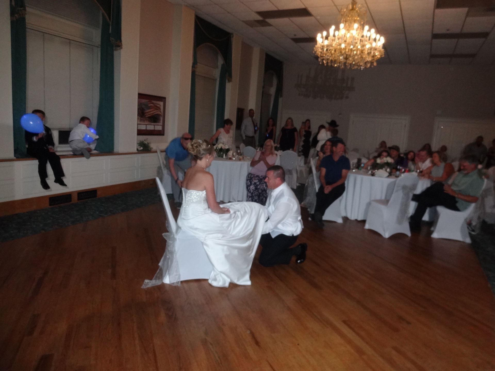 A bride and groom are kneeling down in front of a crowd at their wedding reception
