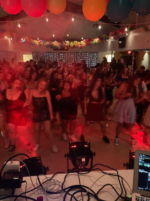 A large group of people are dancing in a room with balloons hanging from the ceiling
