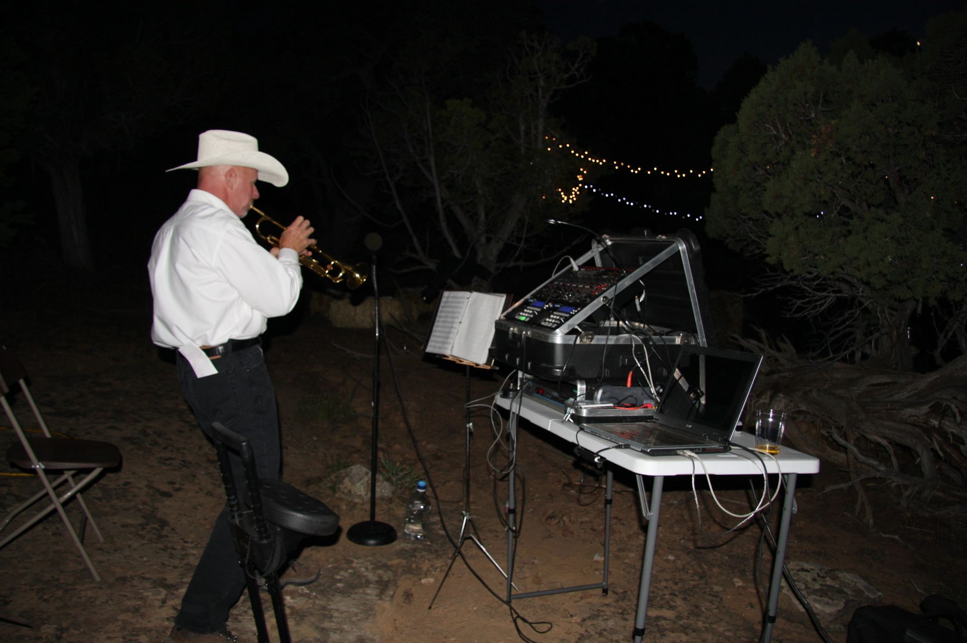 A man in a cowboy hat is playing a trumpet outside at night.