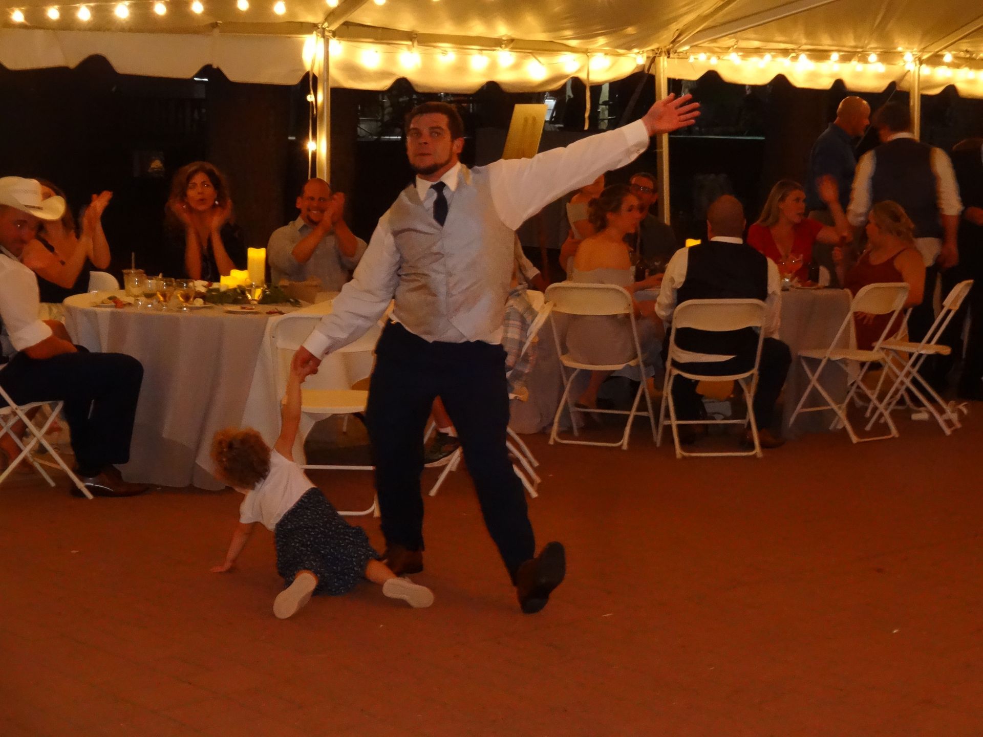 A man is holding a child 's hand while dancing at a wedding reception