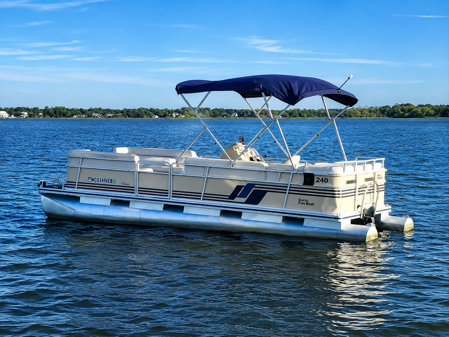Pontoon boat with blue canopy on calm lake under a clear sky