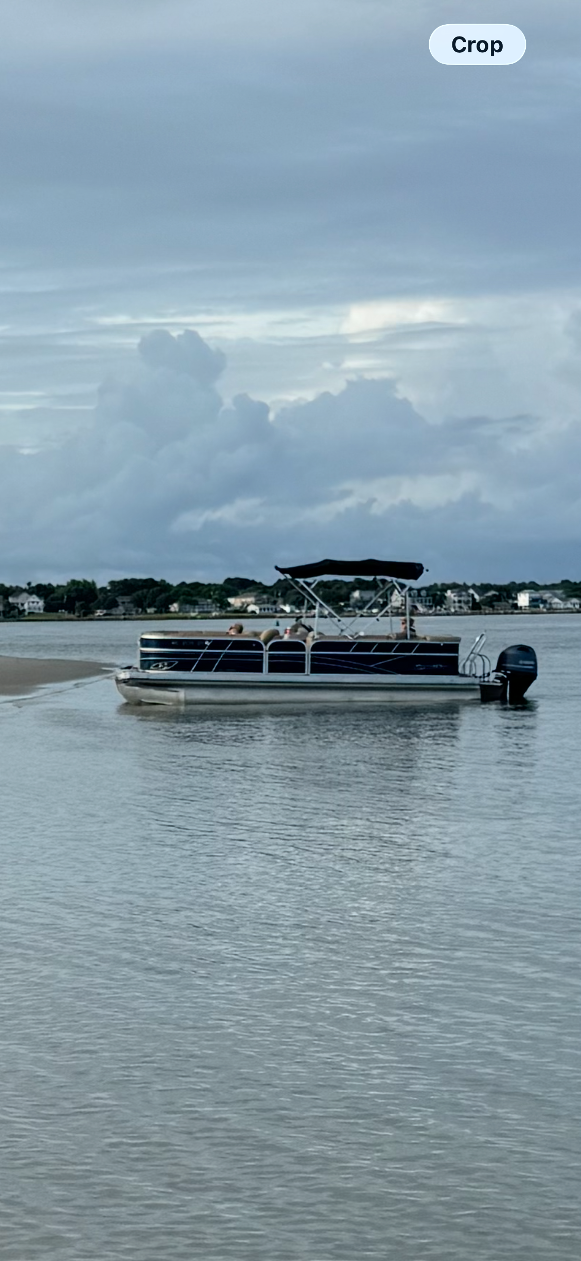 Boat near a sandy beach with people swimming, a folding chair on shore, and striped umbrellas under a blue sky