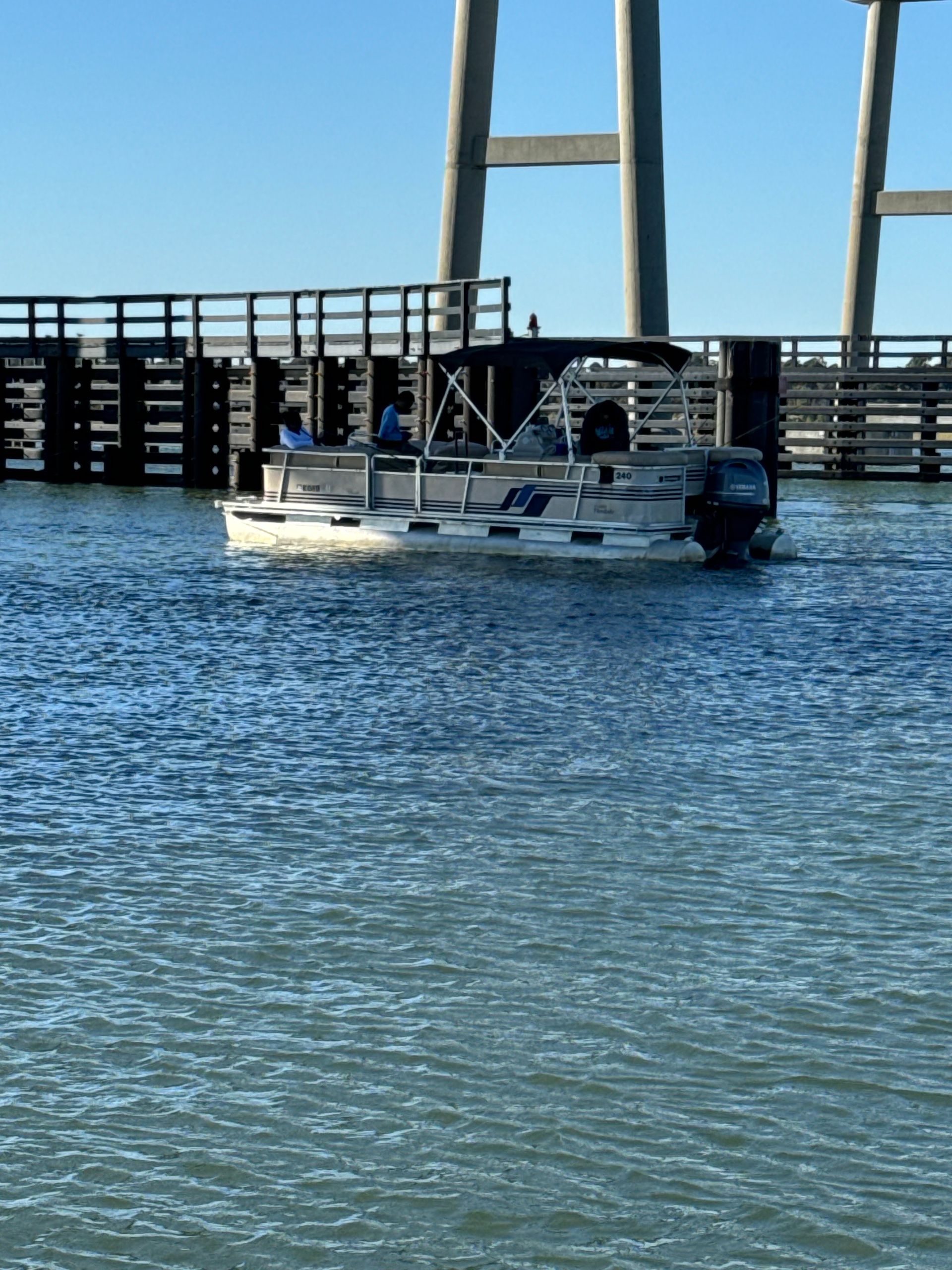 Two white boats on calm water near a bridge and wooden pier under a clear blue sky