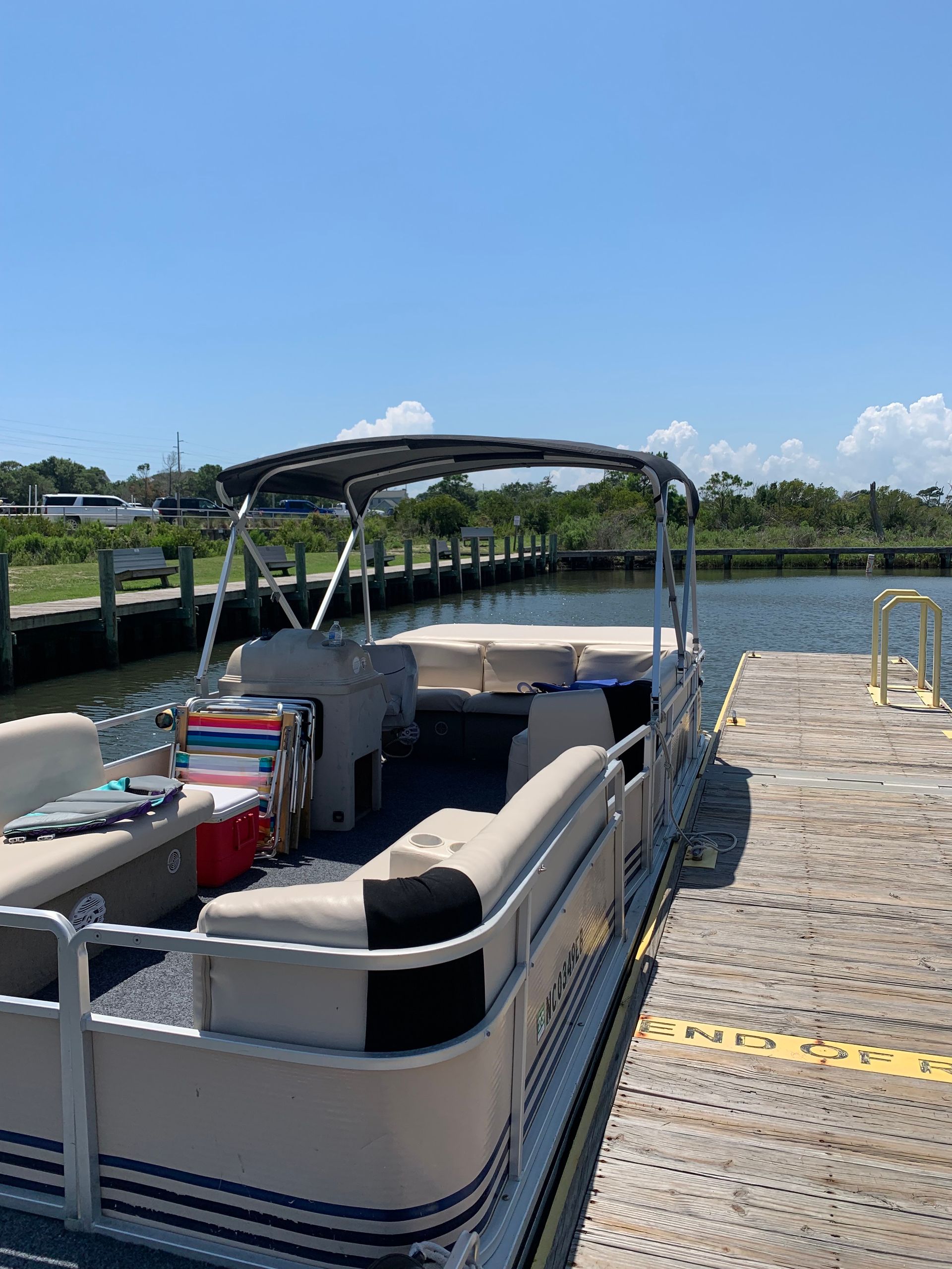 Pontoon boat docked at a sunny marina with calm water and a wooden pier