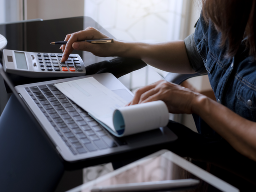A woman is sitting at a table using a laptop and a calculator.