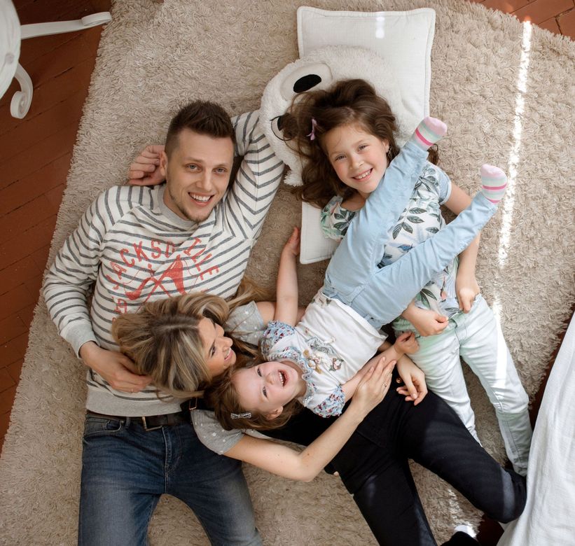 Four people lying on a carpet, smiling and relaxing together indoors.
