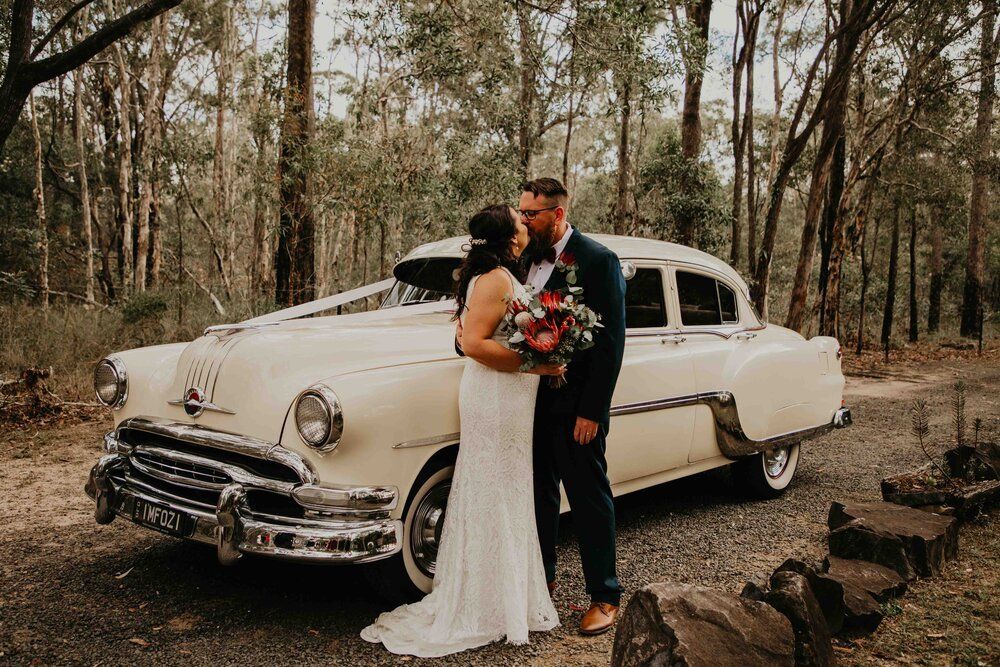 Bride And Groom Kissing In Front Of Classic Car — Classic Car Hire in Dundowran Beach, QLD