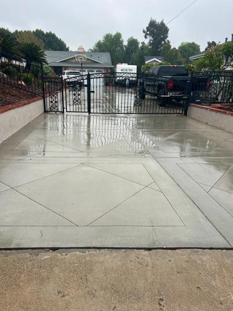 A concrete driveway with a gate and a fence in front of a house.