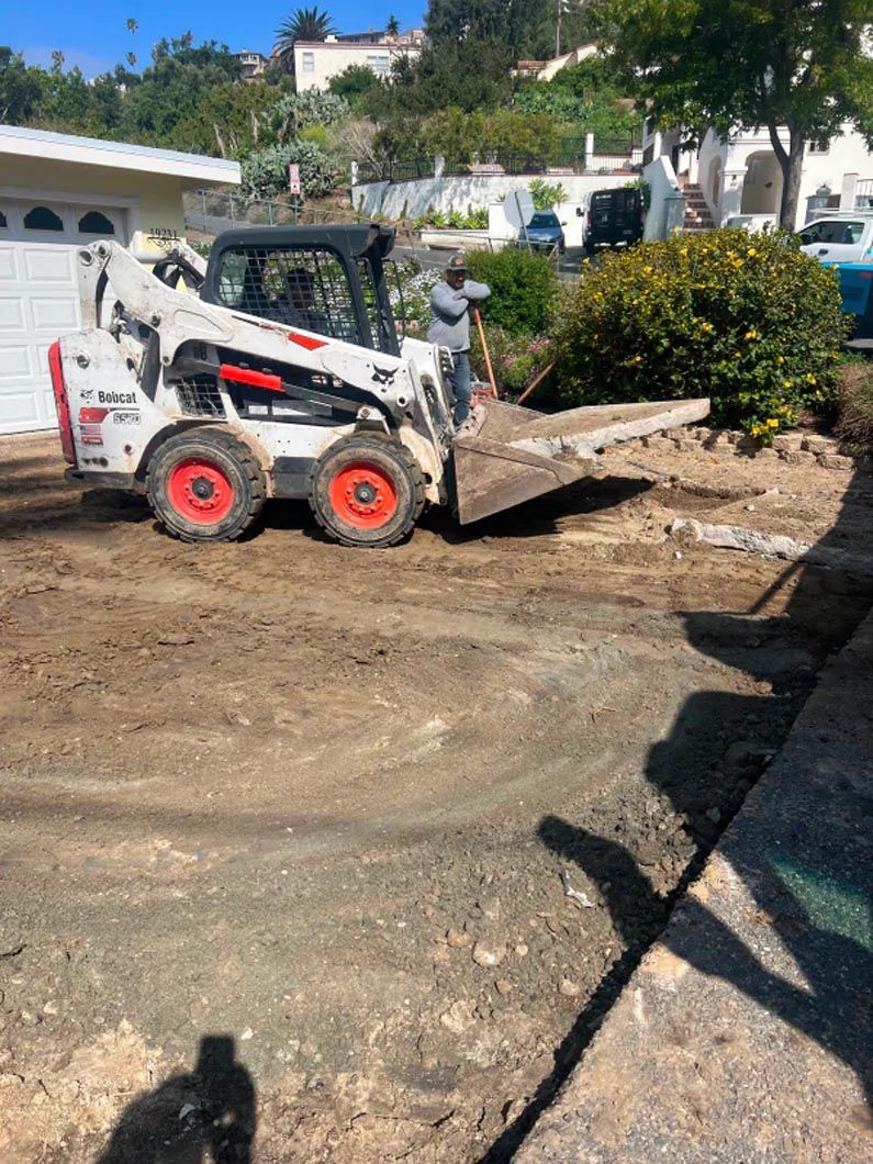 A bobcat is moving dirt in a driveway in front of a house.